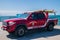 Bright red Huntington Beach fire and lifeguard rescue pickup truck with surfboards on the top rack parked on the pier