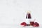 Bright red pomegranate juice in glass bottle mock up with blank label, straw, wine glass, fruit grains on white wood table.