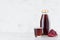 Bright red pomegranate juice in glass bottle mock up with wine glass, fruit grains on white wood table in light interior, template