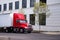 Bright red semi truck with semi trailer on city street with multilevel building