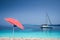 Bright red striped sun beach umbrella on pebble beach against turquoise blue shellow sea water and clean blue sky. White