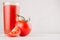 Bright red tomato juice in elegance glass with glossy tomato and ripe piece closeup on white wooden board.