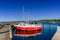 Bright red and white sailboat in a marina with darl blue water under a blue sky