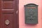 A bright retro looking green mailbox, or letterbox, affixed to the exterior wall of a pink house. There`s a brown door with gold