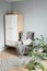 Bright room in Scandinavian style: gray armchair with a plaid and pillows, a white wardrobe, white chair, a rug and green flowers