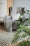 Bright room in Scandinavian style: gray armchair with a plaid and pillows, a white wardrobe, white chair, a rug and green flowers