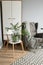 Bright room in Scandinavian style: gray armchair with a plaid and pillows, a white wardrobe, white chair, a rug and green flowers