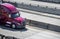 Bright shiny big rig purple semi truck transporting cargo in semi trailer moving on the divided highway intersection with concrete