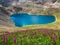 Bright summer azure mountain lake among black rocks. Blue alpine lake among sunlit black green rocky flower hills in highlands