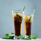 Bright summer fresh cocktail of cola with ice in two glasses with mint and lime in dark grey modern interior, closeup.