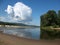 Bright sunny day. Calm river, sandy beach. Blue sky, big cloud