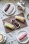 Bright tasty eclairs of different colors on plates and blackboard, summer dessert menu on a gray concrete table