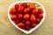 Bright tomatoes red juicy vegetables in a white basket heart shape close-up on a wooden background close-up