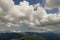 Bright white puffy clouds lit by sun spreading against blue summer sky over green mountain ridge.