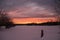 Bright winter sunset over snowy farm pasture with fencepost