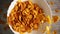 Bright yellow cornflakes for a healthy breakfast fall into a plate close-up and scatter on the table