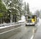 Bright yellow day cab big rig car hauler semi truck with empty semi trailer driving on the winter slippery highway road at snowing