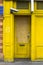 Bright yellow entrance supervised by a video camera. Entry clogged with plywood. The yellow door is closed. Security in europe