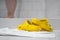 Bright yellow home shoes in rubber slippers style on white towel, on the ceramic floor of bathroom. Human legs having shower on