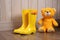 bright yellow kids rubber boots next to a fluffy teddy bear on a wooden floor
