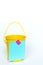 Bright yellow metal pail with aqua colored lined paper taped to front with pink washi tape on solid white background