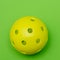 Bright yellow pickleball or whiffle ball on a solid bright green flat lay background symbolizing sports and activity with copy