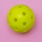 Bright yellow pickleball or whiffle ball on a solid bright pink flat lay background symbolizing sports and activity with copy