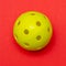 Bright yellow pickleball or whiffle ball on a solid bright red flat lay background symbolizing sports and activity with copy space