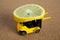 A bright yellow toy forklift carries a slice of lemon. Close-up miniatures on balsa wood background. Modeling