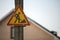 Bright yellow triangular warning sign ;Attention, work ahead, posted high on concrete pillar on blurred house and blue sky copy sp
