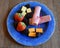 Brightly colored plate with fruit, sausage and cheese on wood background