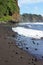 Brightly colored rocks strewn along a black sand beach ending in a cliffside and meeting the Pacific Ocean in Hawaii