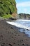 Brightly colored rocks strewn along a black sand beach ending in a cliffside and meeting the Pacific Ocean in Hawaii