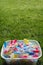 Brightly coloured clothes pegs in a bucket on green grass in sun