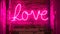 A brightly illuminated neon sign that spells out the word love hangs on a weathered brick wall, Bright pink neon sign reading Love