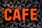 Brightly lit neon sign in the shape of the word "Cafe" surrounded by a bold black triangle pattern