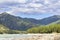 Brightly lit pebble beach, green mountain river Katun, forest, Altai mountains and blue cloudy sky