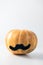 Brightly orange pumpkin with black mustache on light white background. Concept of Halloween, autumn festivals, World