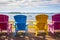 Brightly painted Adirondack chairs of blue, yellow and pink lined up along the bank of the St. Lawrence River in Clayton, New York