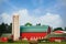A brightly red colored barn with a green roof on a summer day.