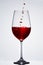 Brightly red wine poured in the fragile pure wineglass standing against light background with reflection in down.