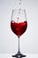 Brightly red wine poured in the fragile pure wineglass standing against light background with reflection in down.