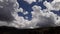 Brilliant and billowy cumulus clouds cluster and cauliflower over the ridge.