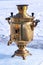 A brilliant samovar stands on an ice plate against a snow background.