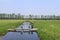 A broad ditch with a big big weir between the green meadows in springtime in holland