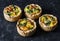 Broccoli cheddar mini savory pies on dark background, top view. Delicious appetizers