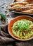 Broccoli hummus with pine nuts, sprouts and olive oil in bowl with croutons over brown wooden background with linen napkin.