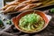 Broccoli hummus with pine nuts, sprouts and olive oil in bowl with croutons over brown wooden background with linen napkin.