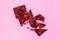 Broken black chocolate bar pieces with scattered dried red berries on pink