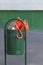 Broken bright orange umbrella in green rubbish bin